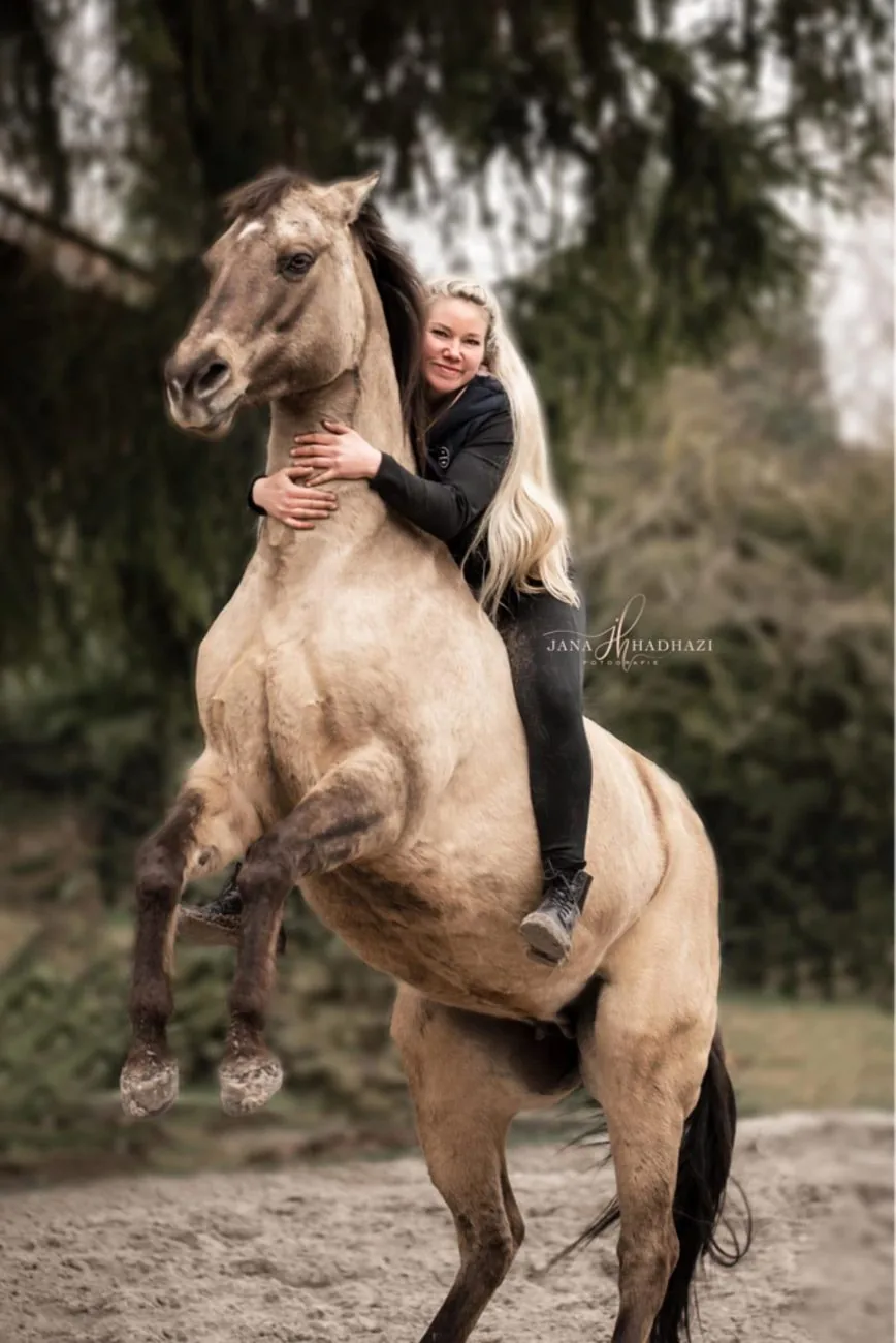 Anne Röder umarmt ihr steigendes Falbenpferd auf dem Reitplatz